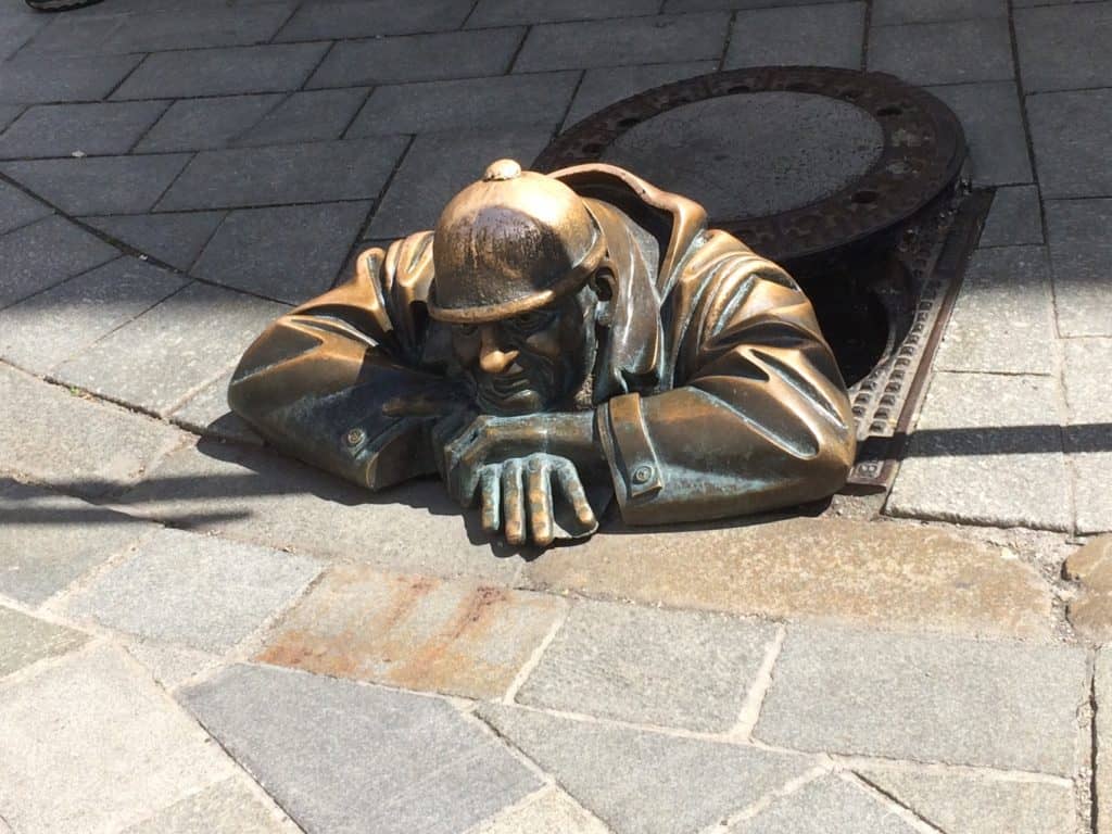Life size bronze statue of a man crawling out from a grid on the street in Bratislava